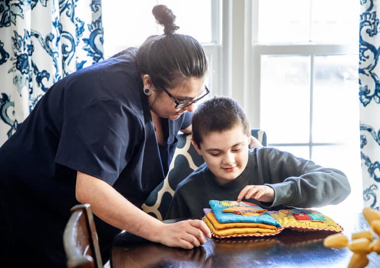 A Caretech caregiver helping a child with a learning activity at home, demonstrating compassionate in-home support for children with chronic conditions and special healthcare needs.