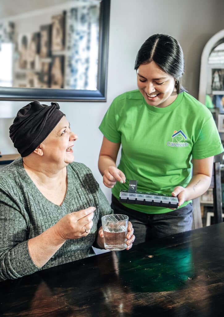 A Caretech caregiver smiling while assisting an adult with a disability at home, highlighting compassionate in-home support that promotes independence and quality of life.